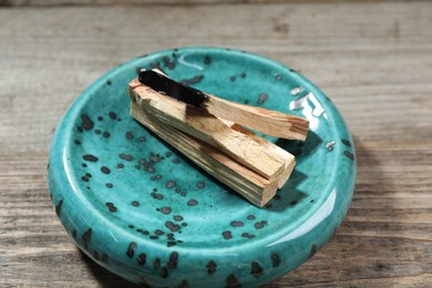 Photo of Palo santo sticks and burnt one on wooden table, closeup