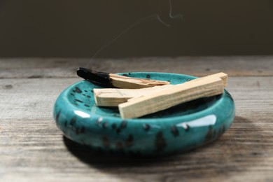 Photo of Palo santo sticks and smoldering one on wooden table against grey background, closeup