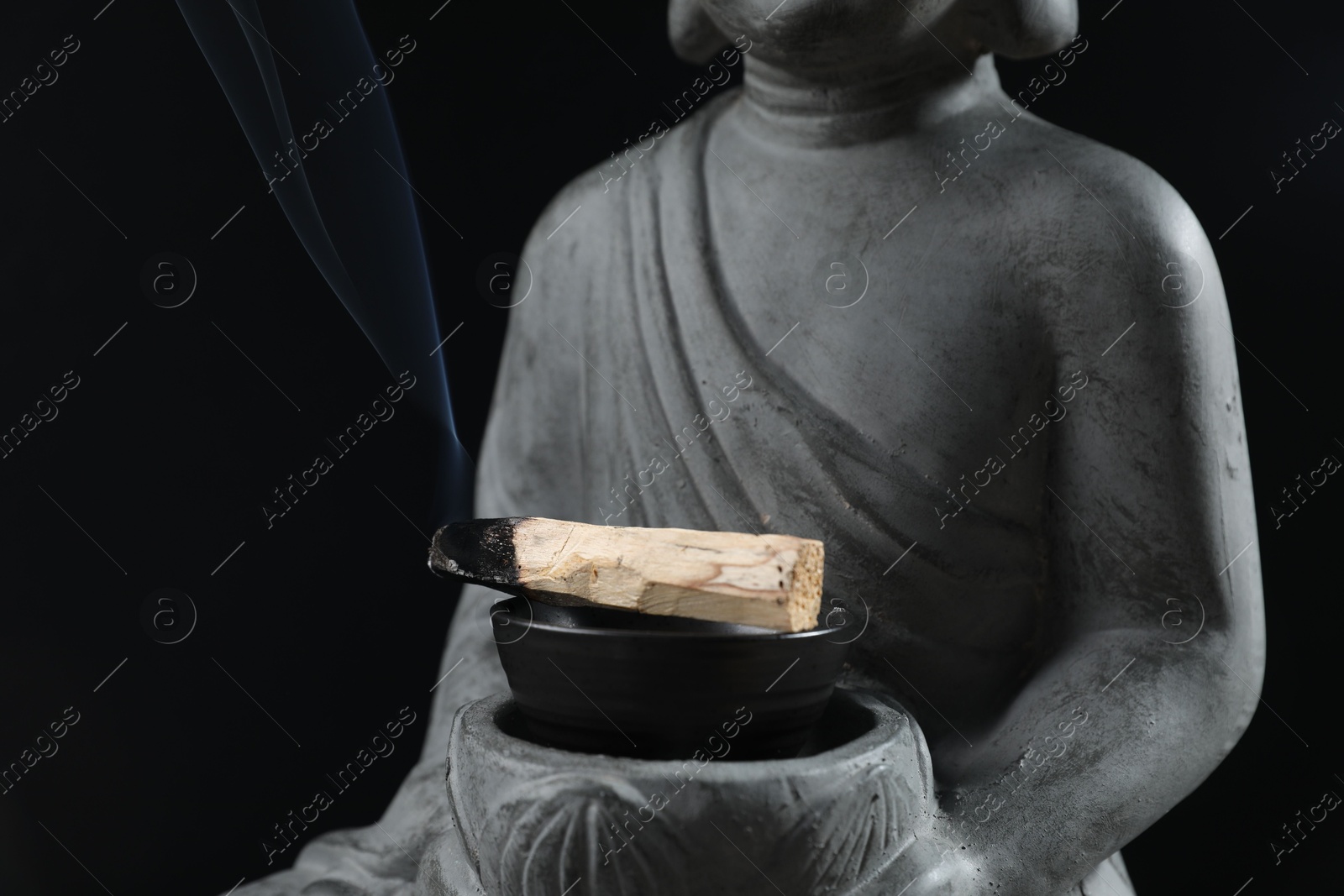 Photo of Smoldering palo santo stick and statue on black background, closeup