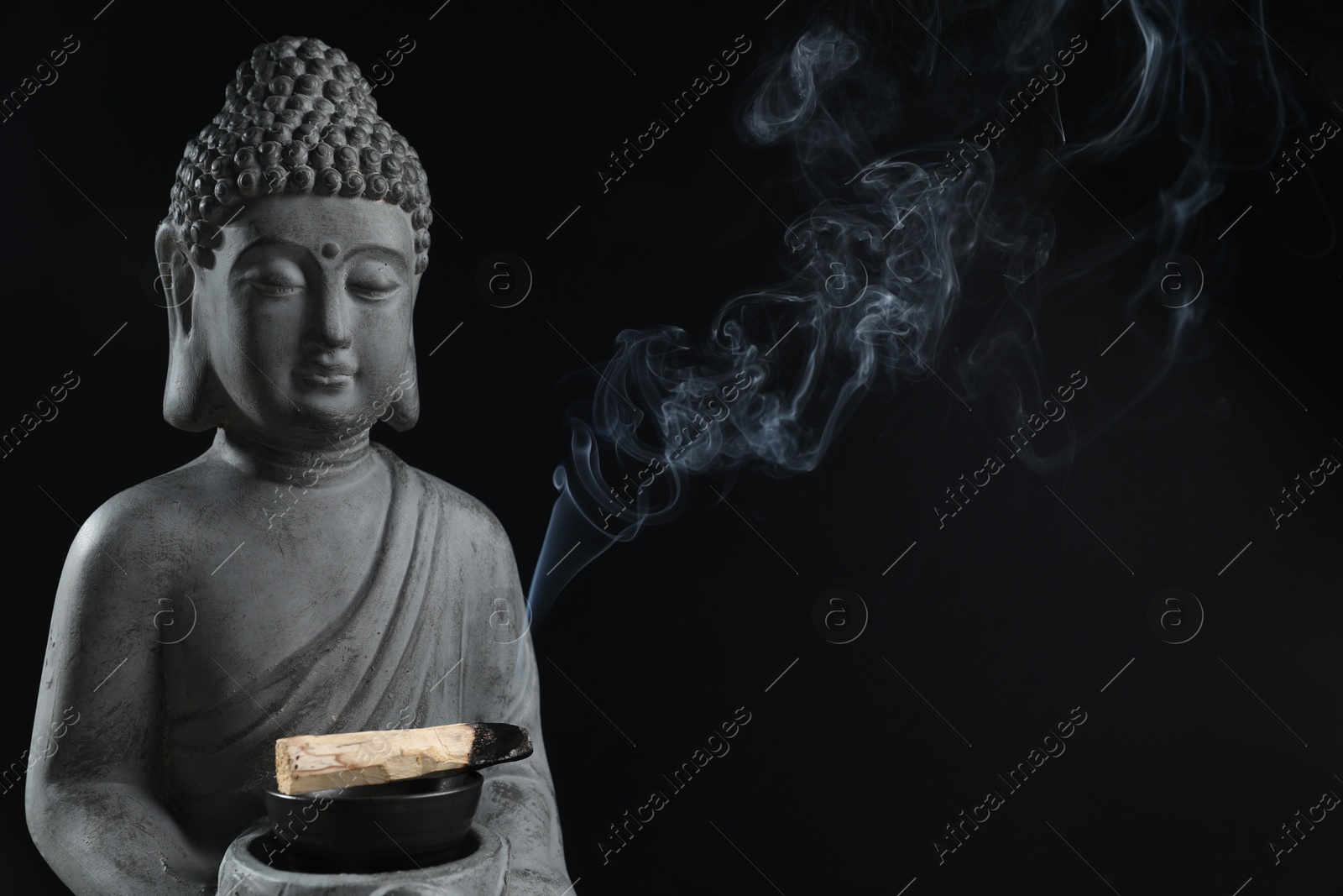 Photo of Smoldering palo santo stick and Buddha statue on black background, closeup. Space for text