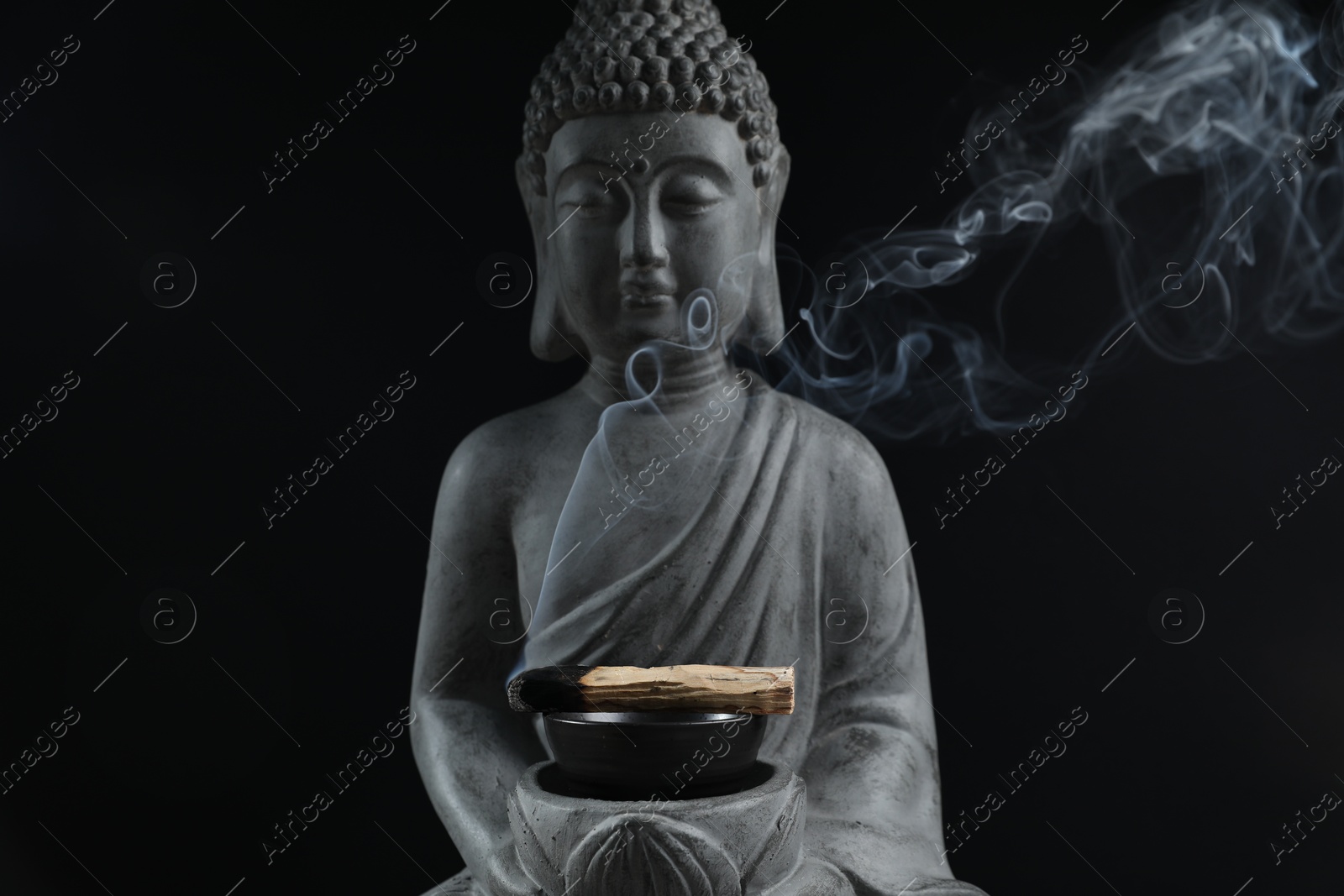 Photo of Smoldering palo santo stick and Buddha statue on black background, closeup