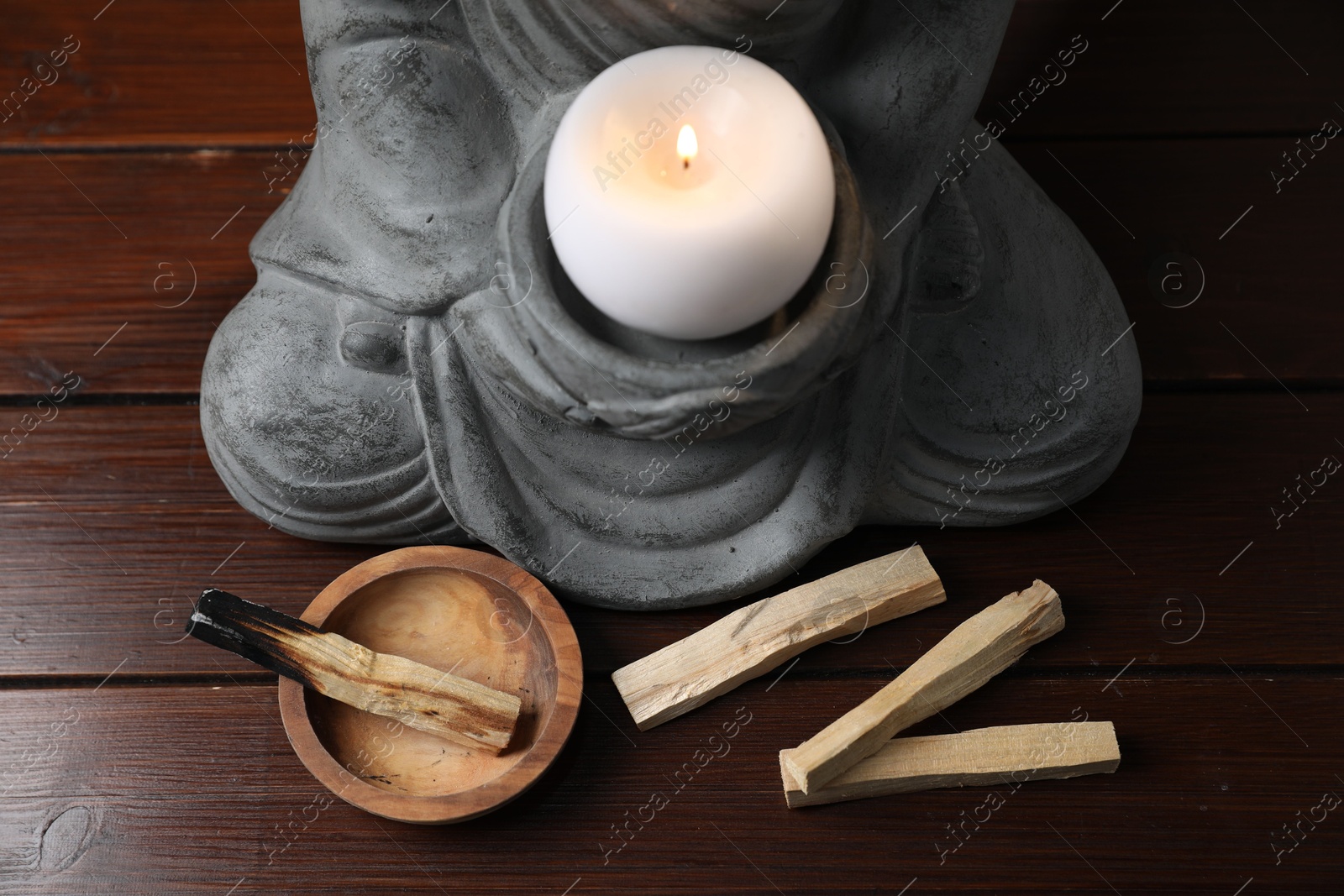 Photo of Palo santo sticks and statue with burning candle on wooden table, closeup