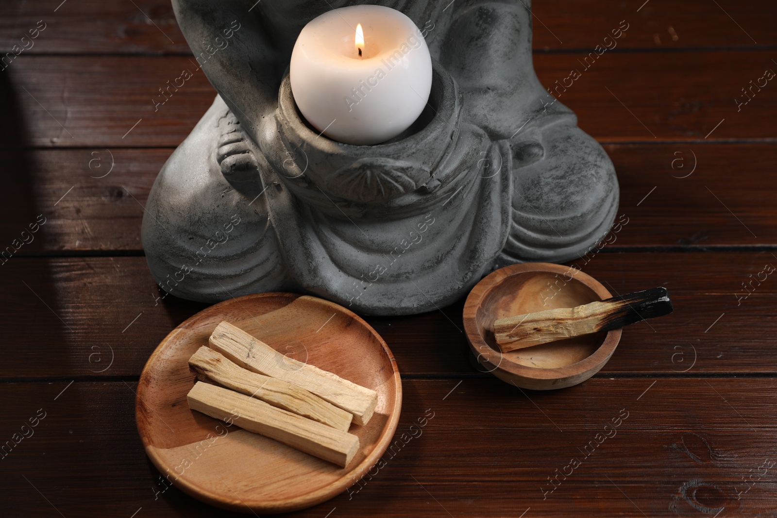 Photo of Palo santo sticks and statue with burning candle on wooden table, closeup