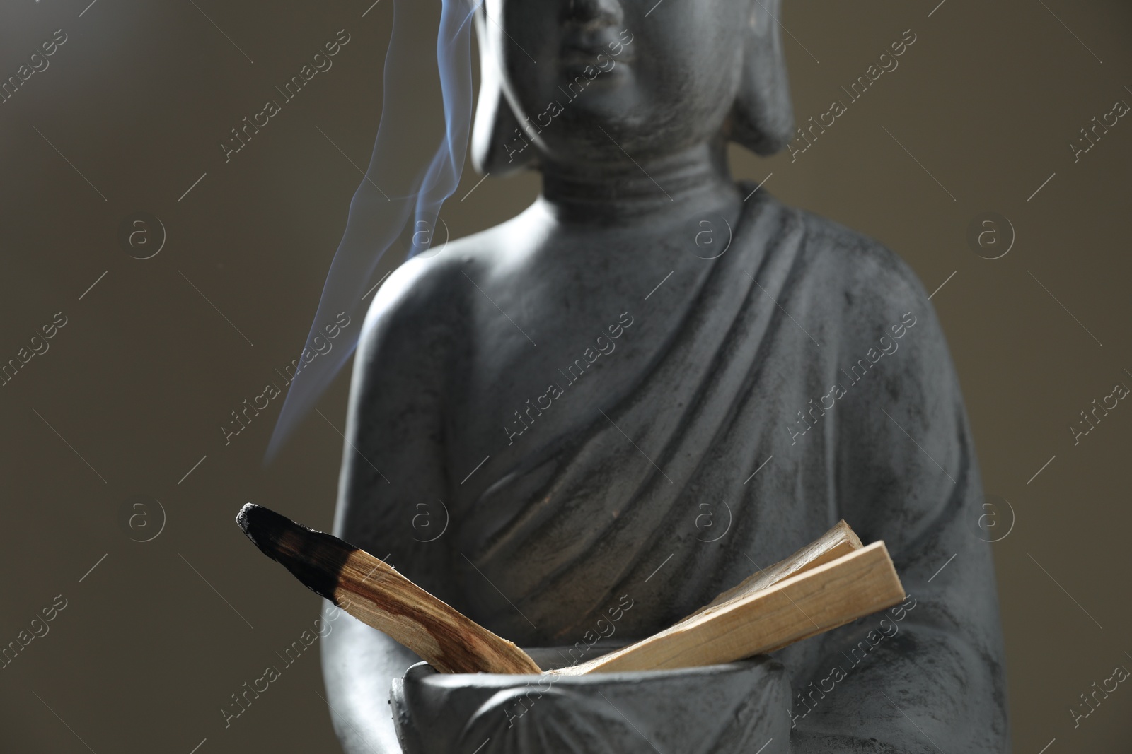 Photo of Smoldering palo santo stick and statue on grey background, closeup