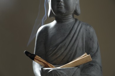 Photo of Smoldering palo santo stick and statue on grey background, closeup