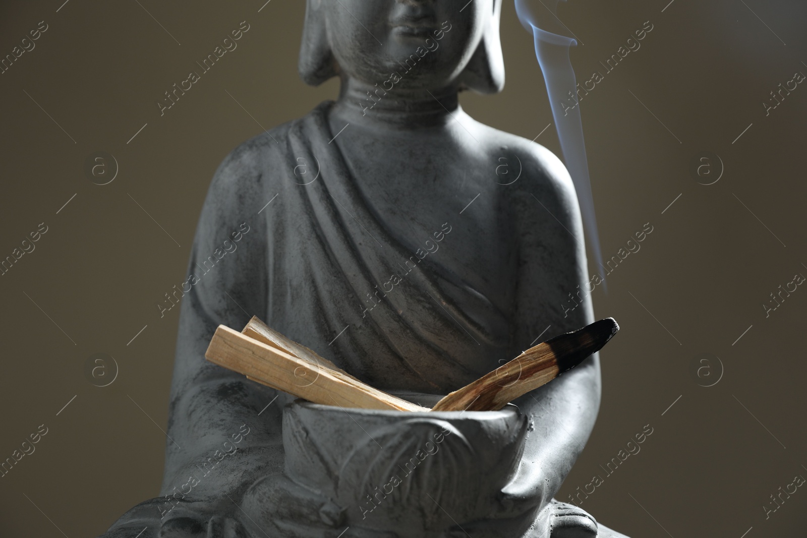 Photo of Smoldering palo santo stick and statue on grey background, closeup