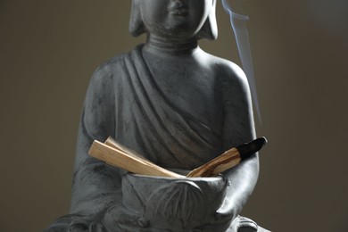 Photo of Smoldering palo santo stick and statue on grey background, closeup