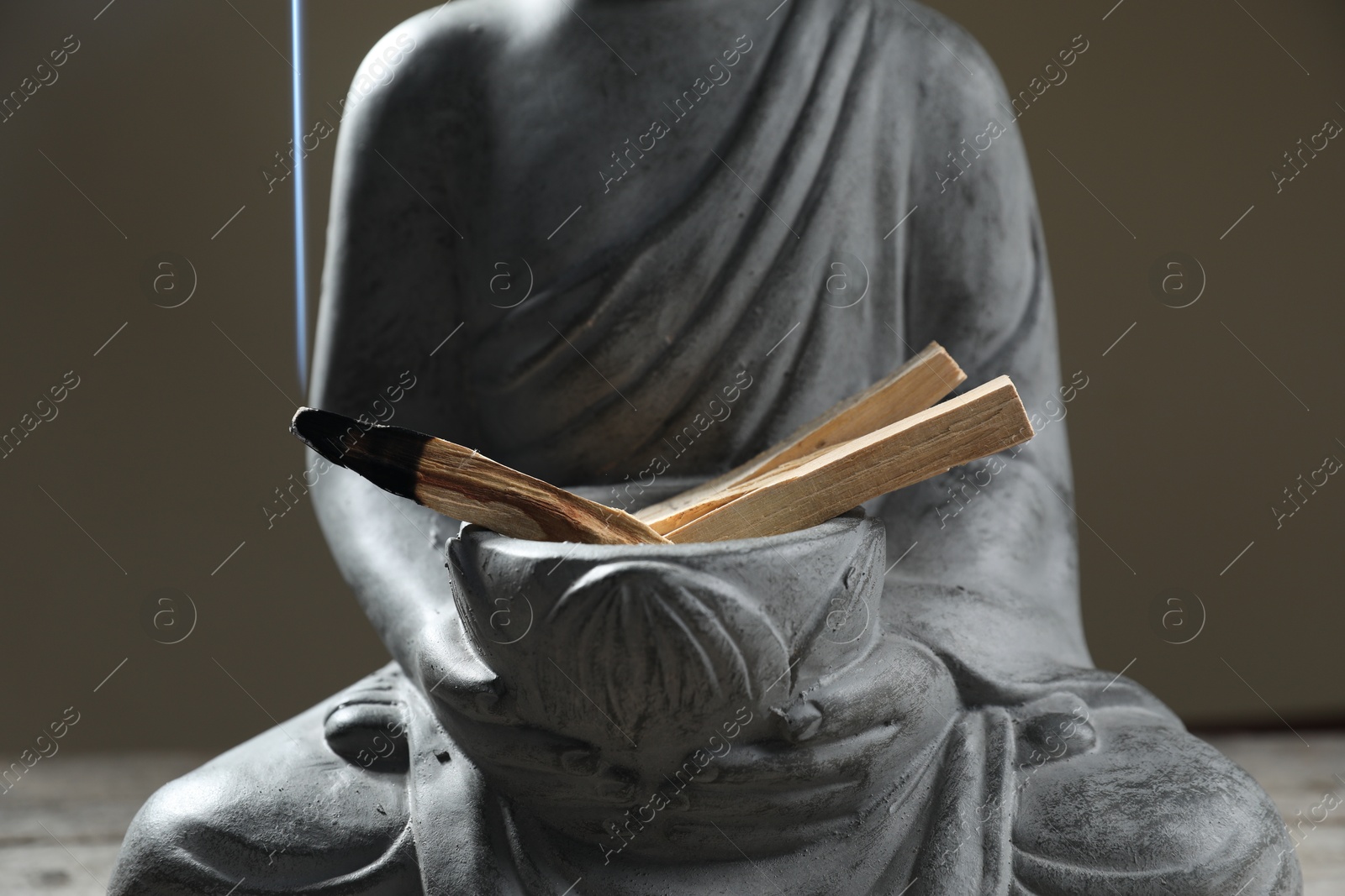 Photo of Smoldering palo santo stick and statue on table against grey background, closeup