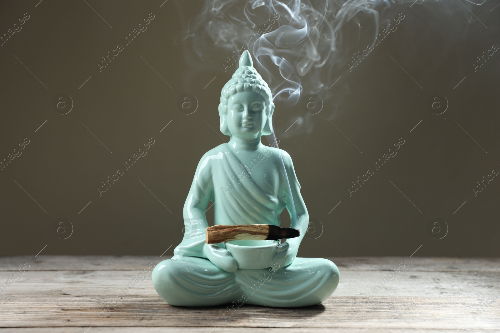 Photo of Smoldering palo santo stick and Buddha statue on wooden table against grey background