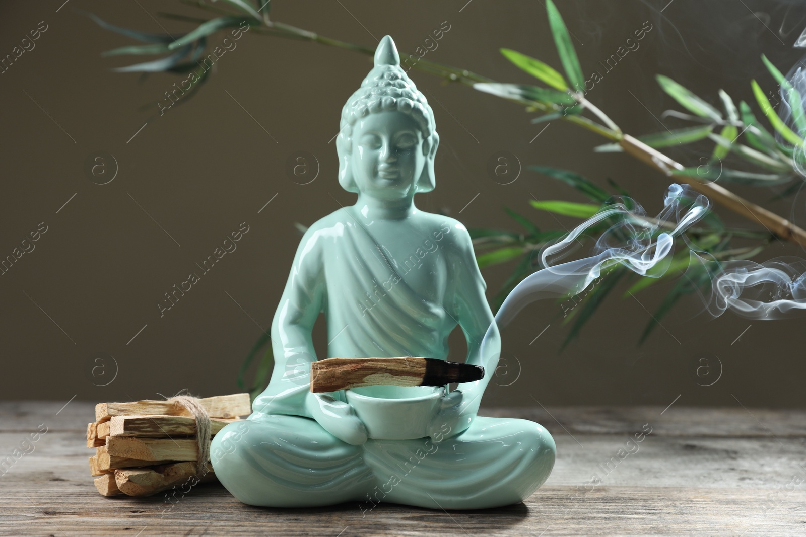 Photo of Smoldering palo santo stick, Buddha statue and beautiful branches on wooden table against grey background