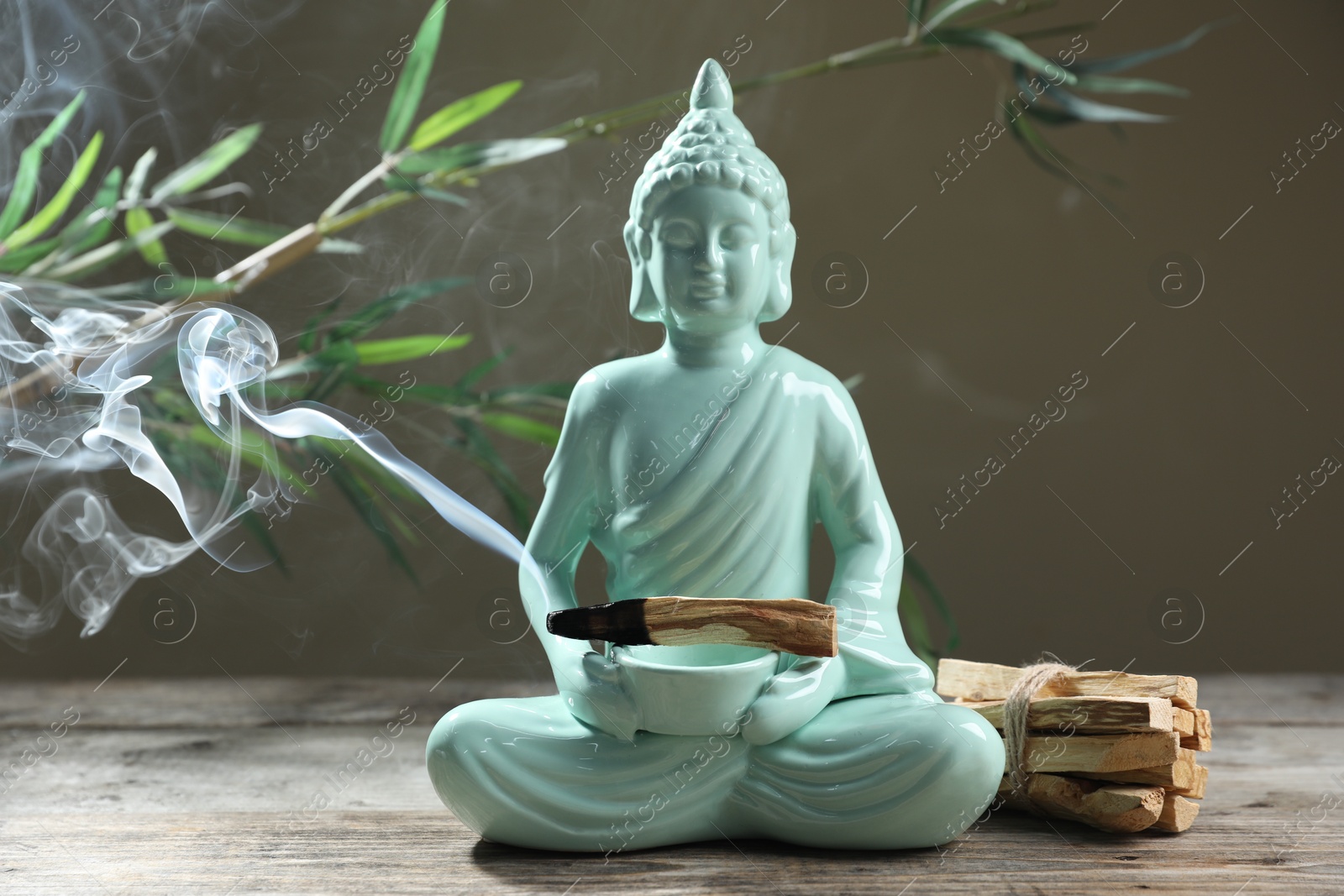 Photo of Smoldering palo santo stick, Buddha statue and beautiful branches on wooden table against grey background