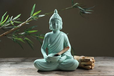 Photo of Burnt palo santo stick, Buddha statue and beautiful branches on wooden table against grey background