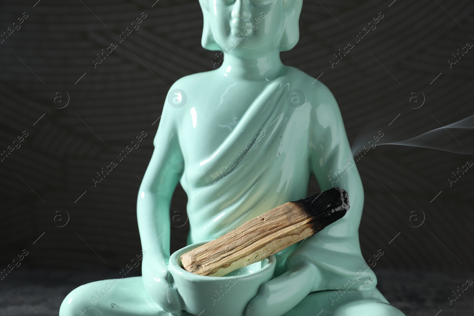 Photo of Smoldering palo santo stick and Buddha statue on black background, closeup