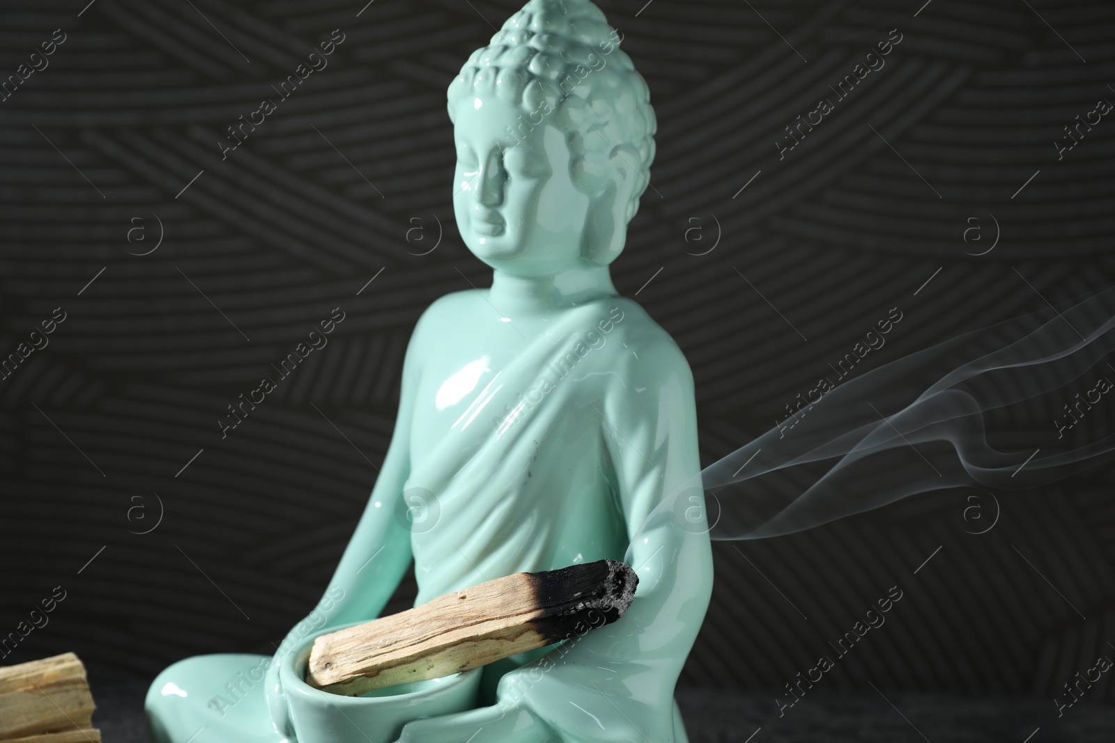 Photo of Smoldering palo santo stick and Buddha statue on black background, closeup