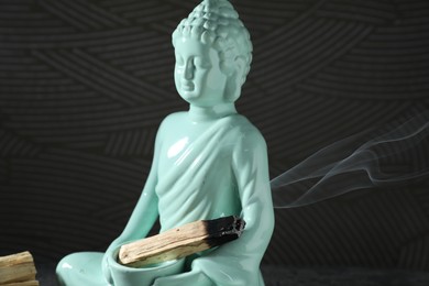 Photo of Smoldering palo santo stick and Buddha statue on black background, closeup