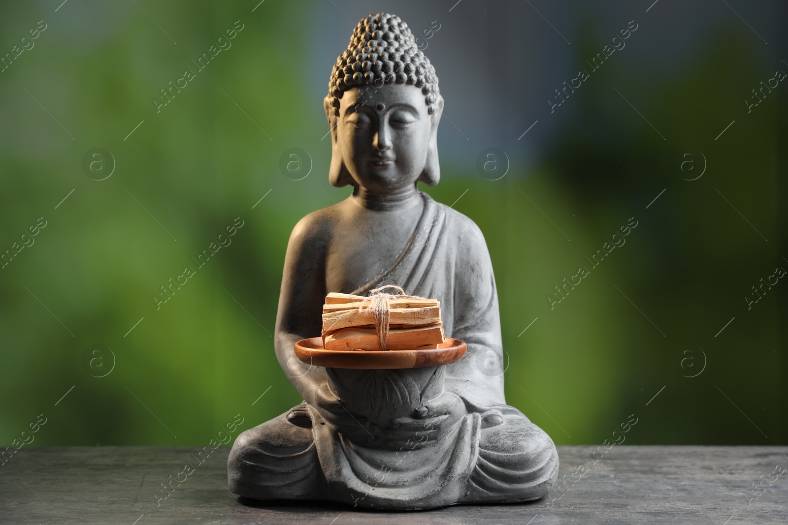 Photo of Bunch of palo santo sticks and Buddha statue on grey textured table against blurred background, closeup