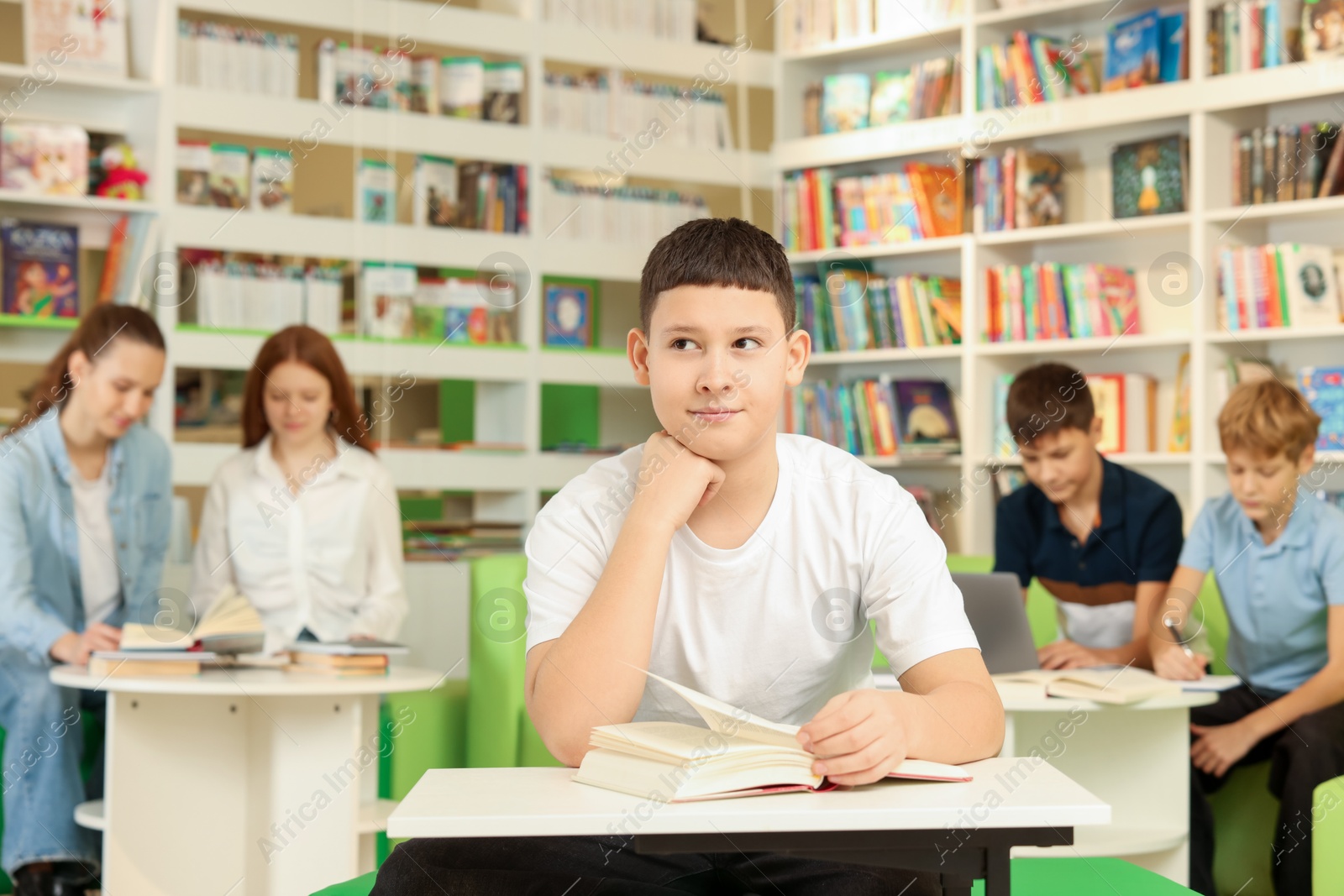 Photo of Teenage boy with book at desk in public library