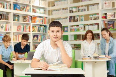 Photo of Teenage boy with book at desk in public library