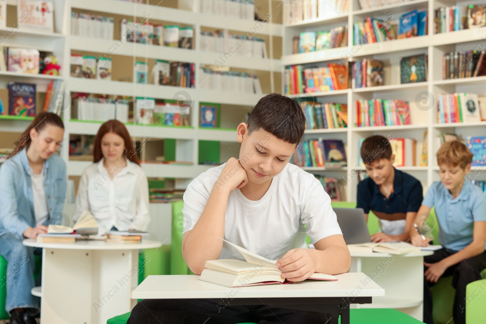 Photo of Teenage boy reading book at desk in public library