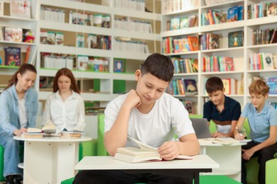 Photo of Teenage boy reading book at desk in public library