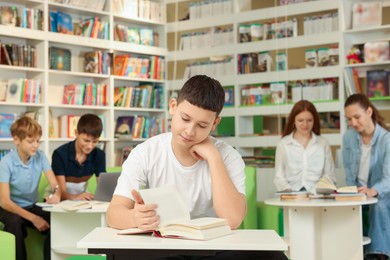 Photo of Teenage boy reading book at desk in public library