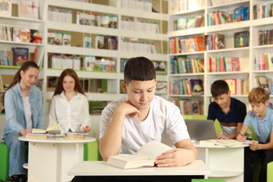 Photo of Teenage boy reading book at desk in public library