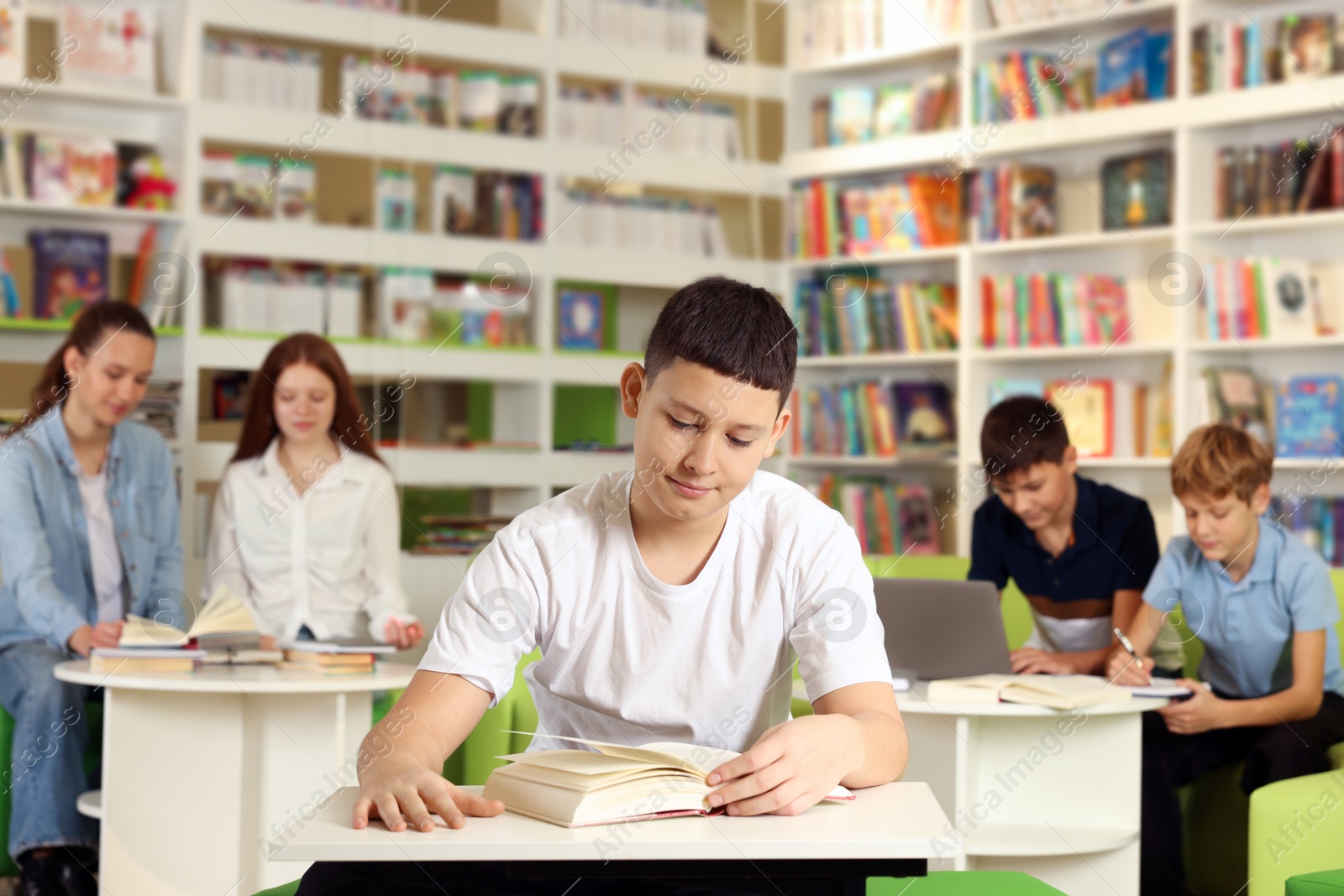 Photo of Teenage boy reading book at desk in public library