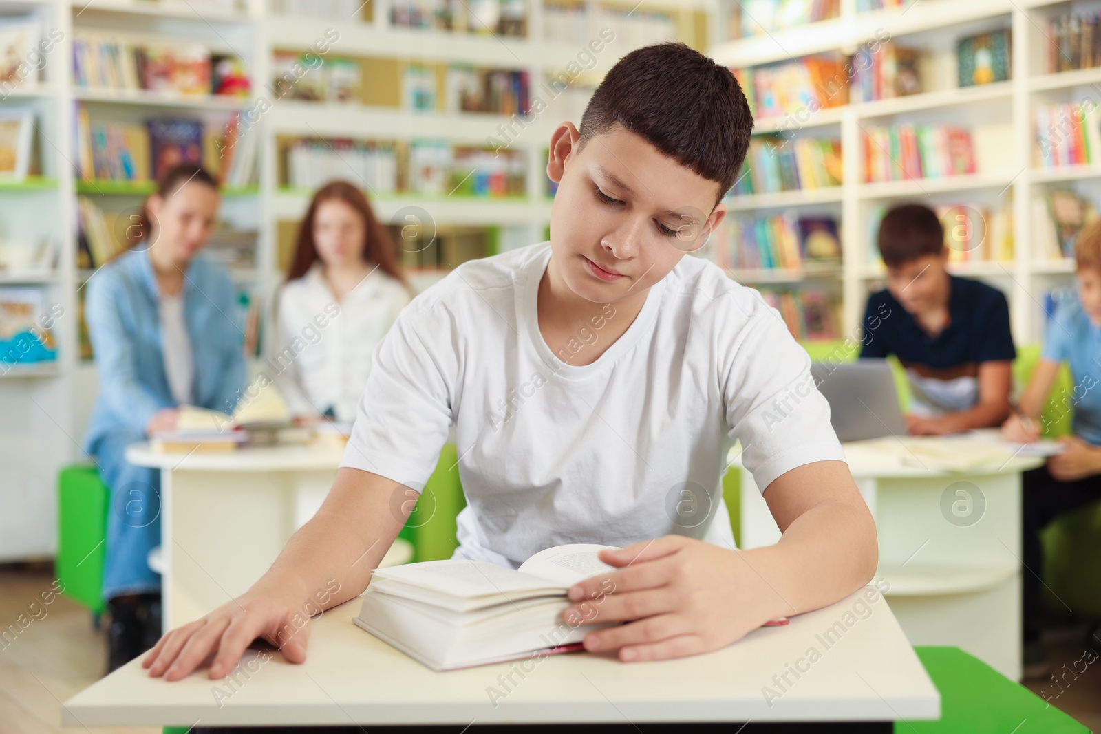 Photo of Teenage boy reading book at desk in public library