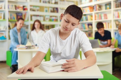 Photo of Teenage boy reading book at desk in public library