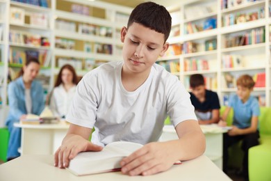 Photo of Teenage boy reading book at desk in public library