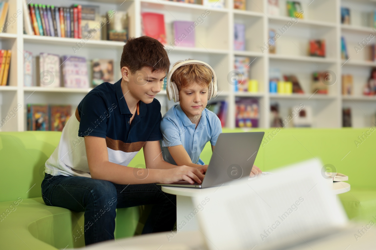 Photo of Teenage friends doing homework with laptop at table in library