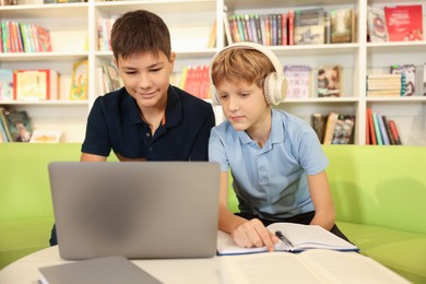 Photo of Teenage friends doing homework with laptop at table in library