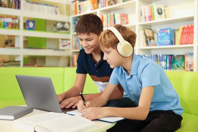 Photo of Teenage friends doing homework with laptop at table in library