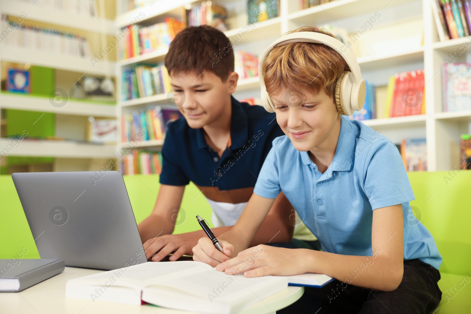 Photo of Teenage friends doing homework with laptop at table in library