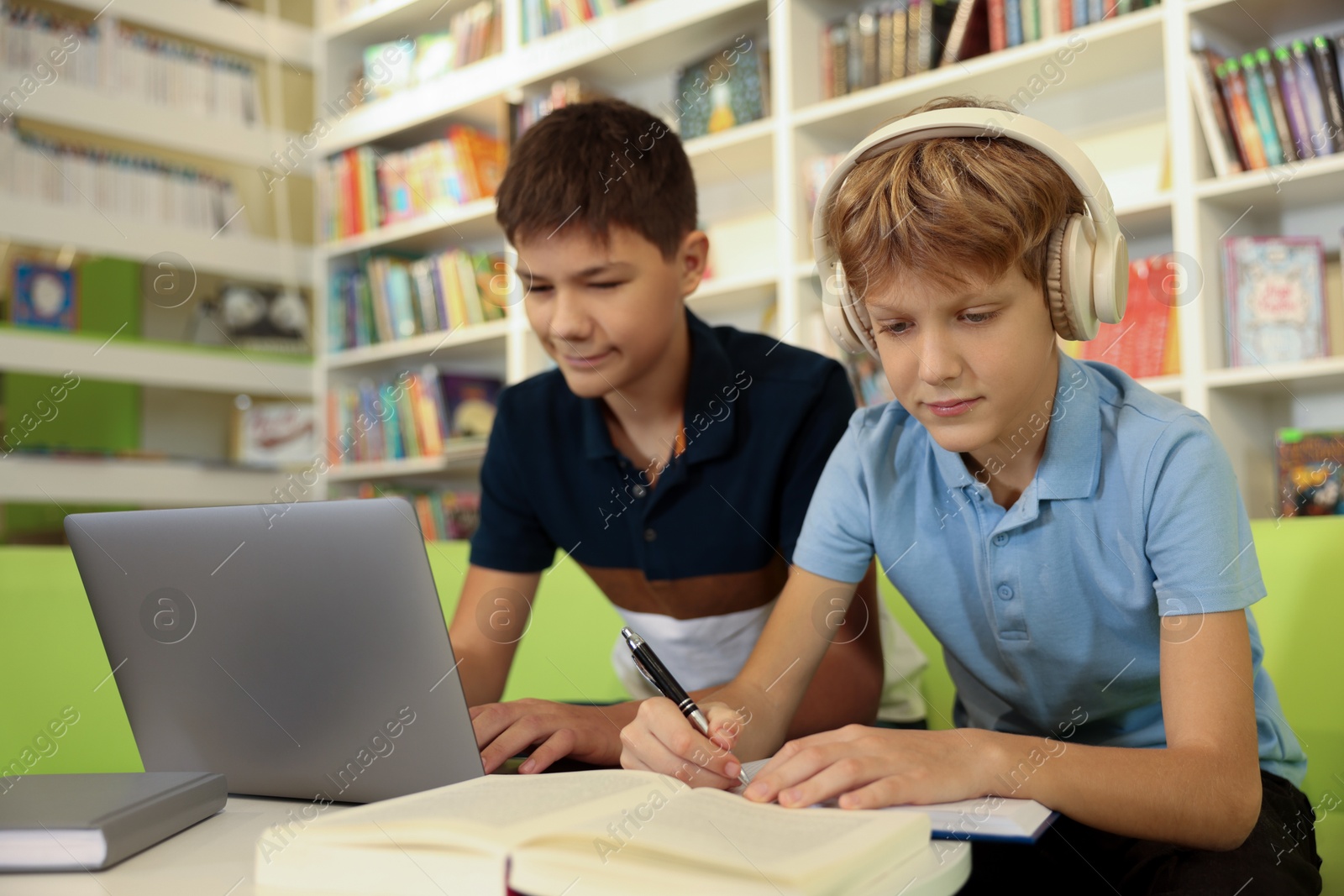 Photo of Teenage friends doing homework with laptop at table in library