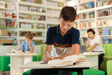 Photo of Teenage boy doing homework at table in public library