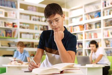 Photo of Teenage boy doing homework at table in public library