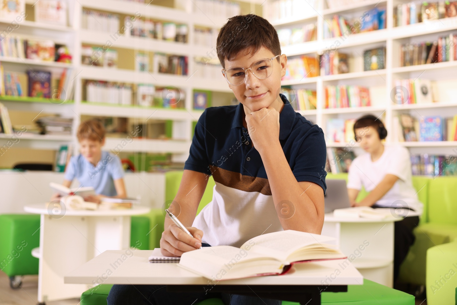 Photo of Teenage boy doing homework at table in public library