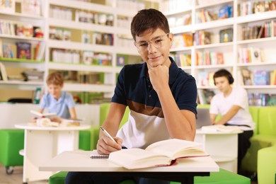 Photo of Teenage boy doing homework at table in public library