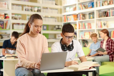 Photo of Teenage friends doing homework with laptop at desk in public library