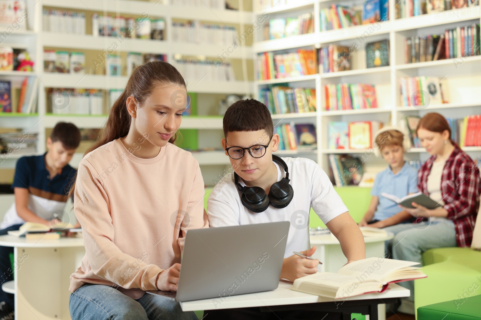 Photo of Teenage friends doing homework with laptop at desk in public library