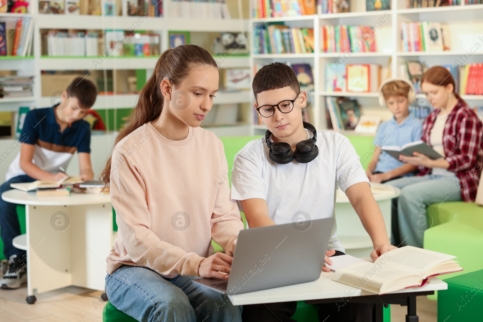 Photo of Teenage friends doing homework with laptop at desk in public library