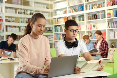 Photo of Teenage friends doing homework with laptop at desk in public library