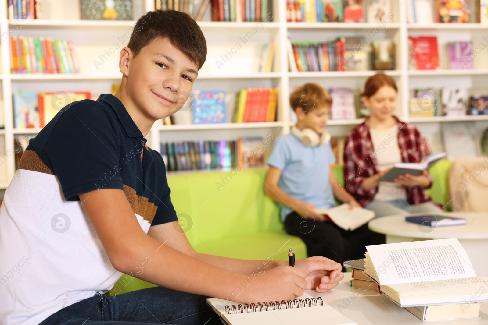 Photo of Teenage boy doing homework at table in public library