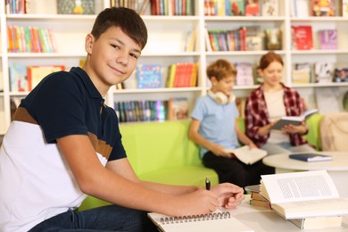 Photo of Teenage boy doing homework at table in public library