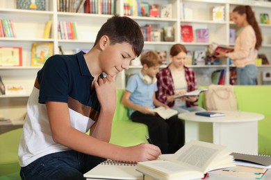 Photo of Teenage boy doing homework at table in public library