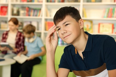 Photo of Thoughtful teenage boy in public library. Space for text