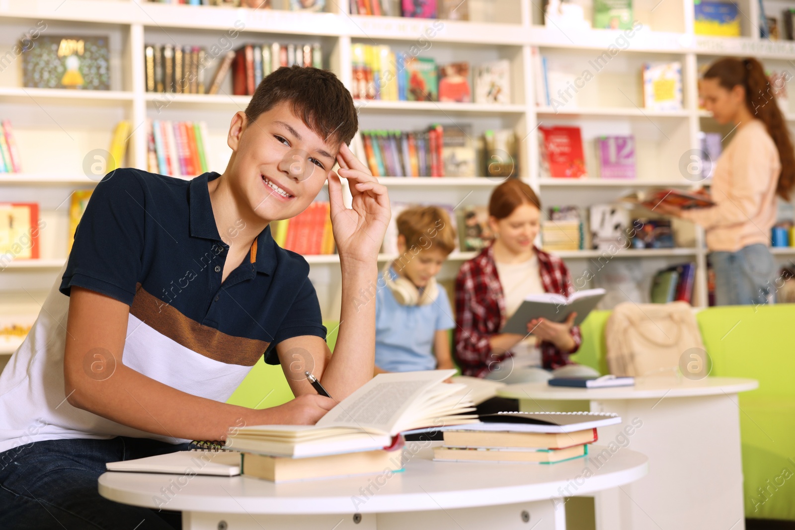 Photo of Smiling teenage boy doing homework at table in public library