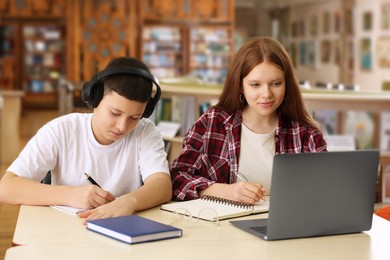 Photo of Teenage friends with laptop doing homework at desk in library