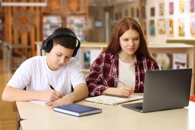 Photo of Teenage friends with laptop doing homework at desk in library